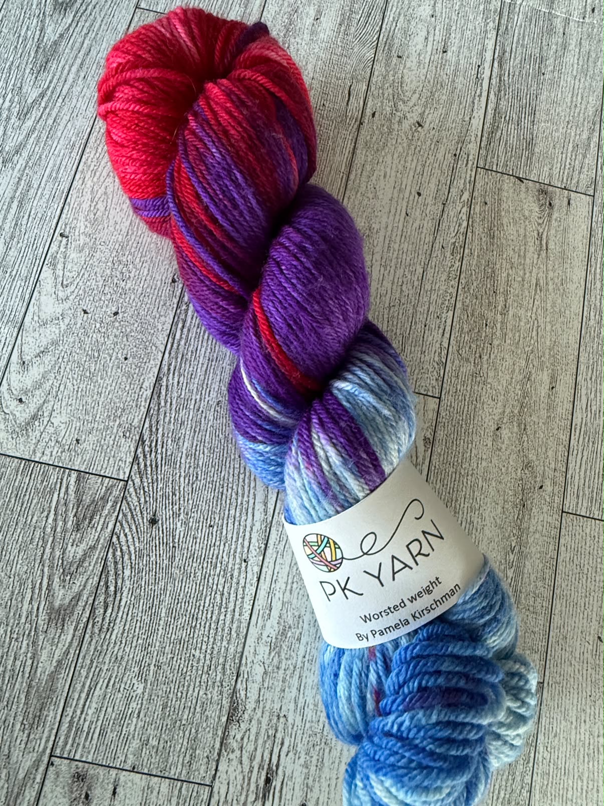 A bright skein of hand-dyed worsted weight yarn from PK Yarn in red, purple, and blue tones