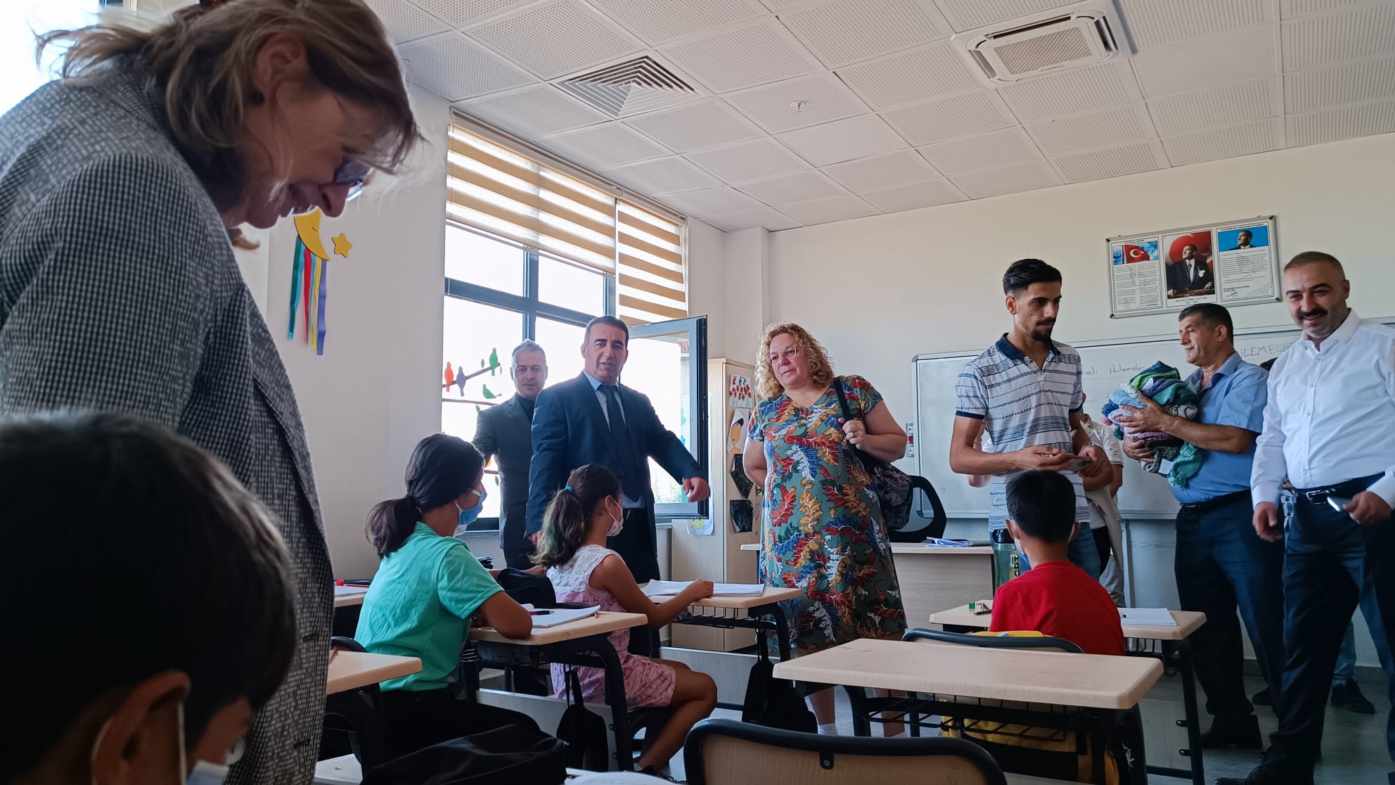 A classroom of students at desks while volunteers and school staff distribute knitwear